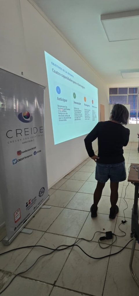 Una relatora de CREIDE presenta una diapositiva con las cuatro capacidades, junto al pendón de la organización.