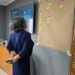 Una relatora observa un papelógrafo con las columnas Tensión, Hostilidad y Agresión, junto a una pantalla con el título “El mapa de la tensión”.